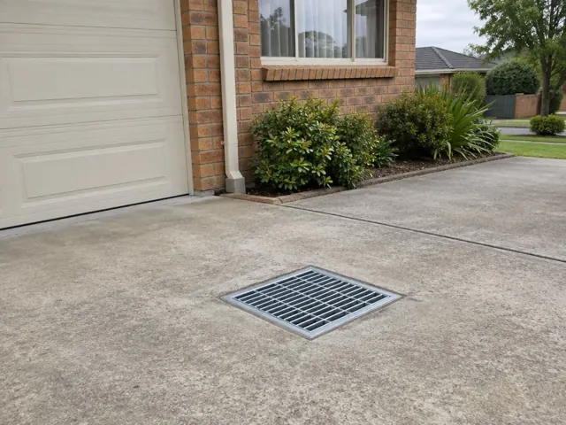 Dry driveway with a clean outdoor drain grate beside a brick house in Jamisontown