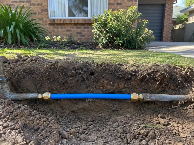 Repaired blue water pipe section in a garden trench beside a brick house in Emu Plains